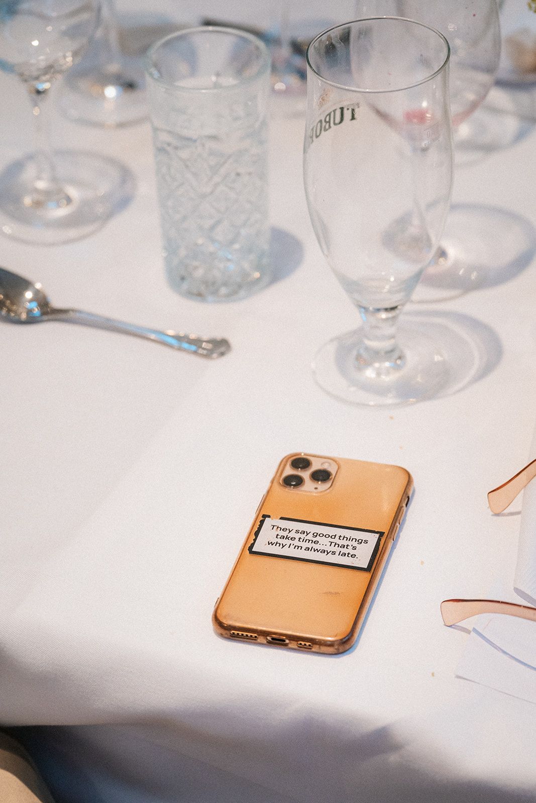 White tablecloth with empty wine glasses and a rose gold iPhone visible on the surface.