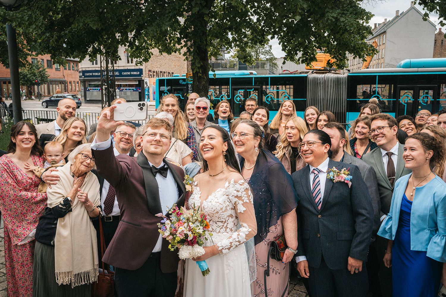 A joyful outdoor wedding celebration with guests gathered closely together smiling and laughing on a summer day.