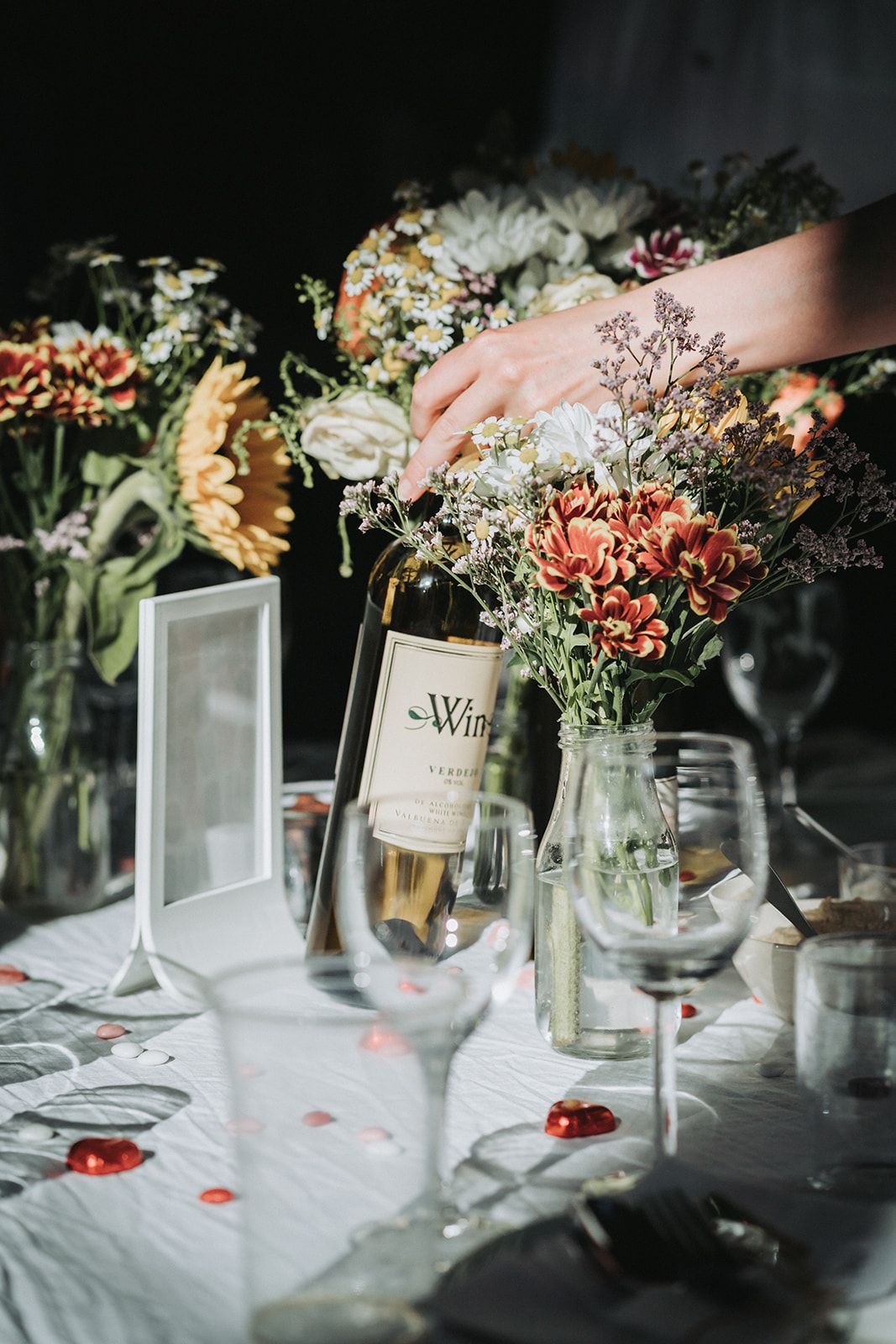 Close-up of elegant wedding table centerpieces with wine bottles and delicate floral arrangements on white linens.