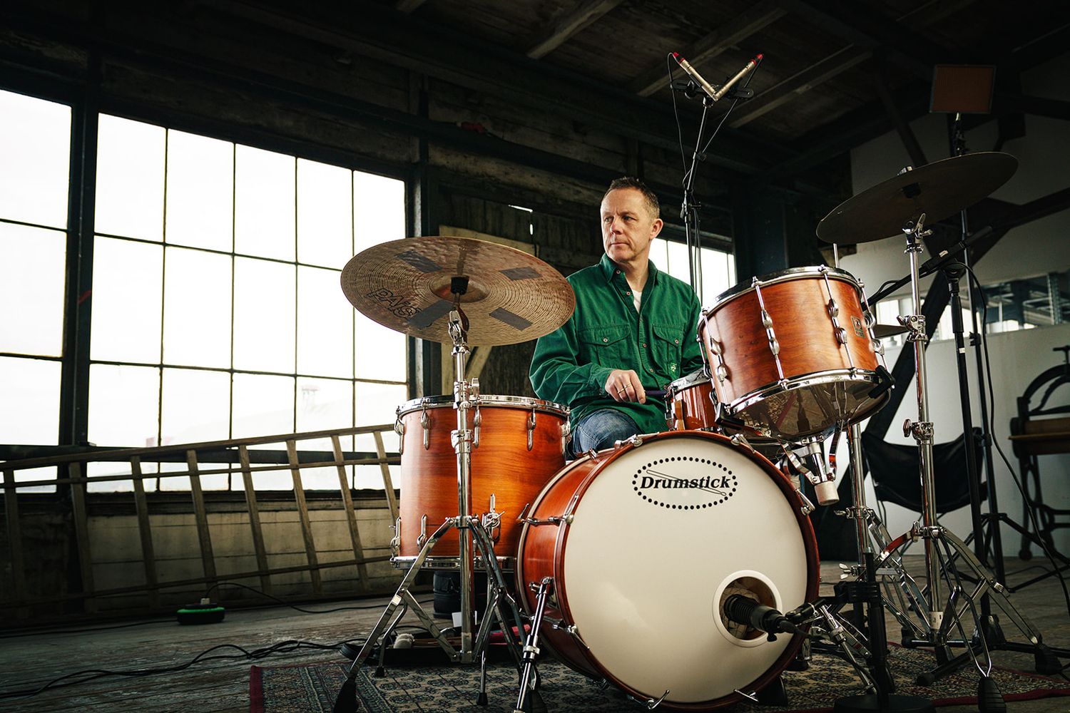 A drum kit setup in a bright industrial space features orange and wooden finishes and vintage style hardware.
