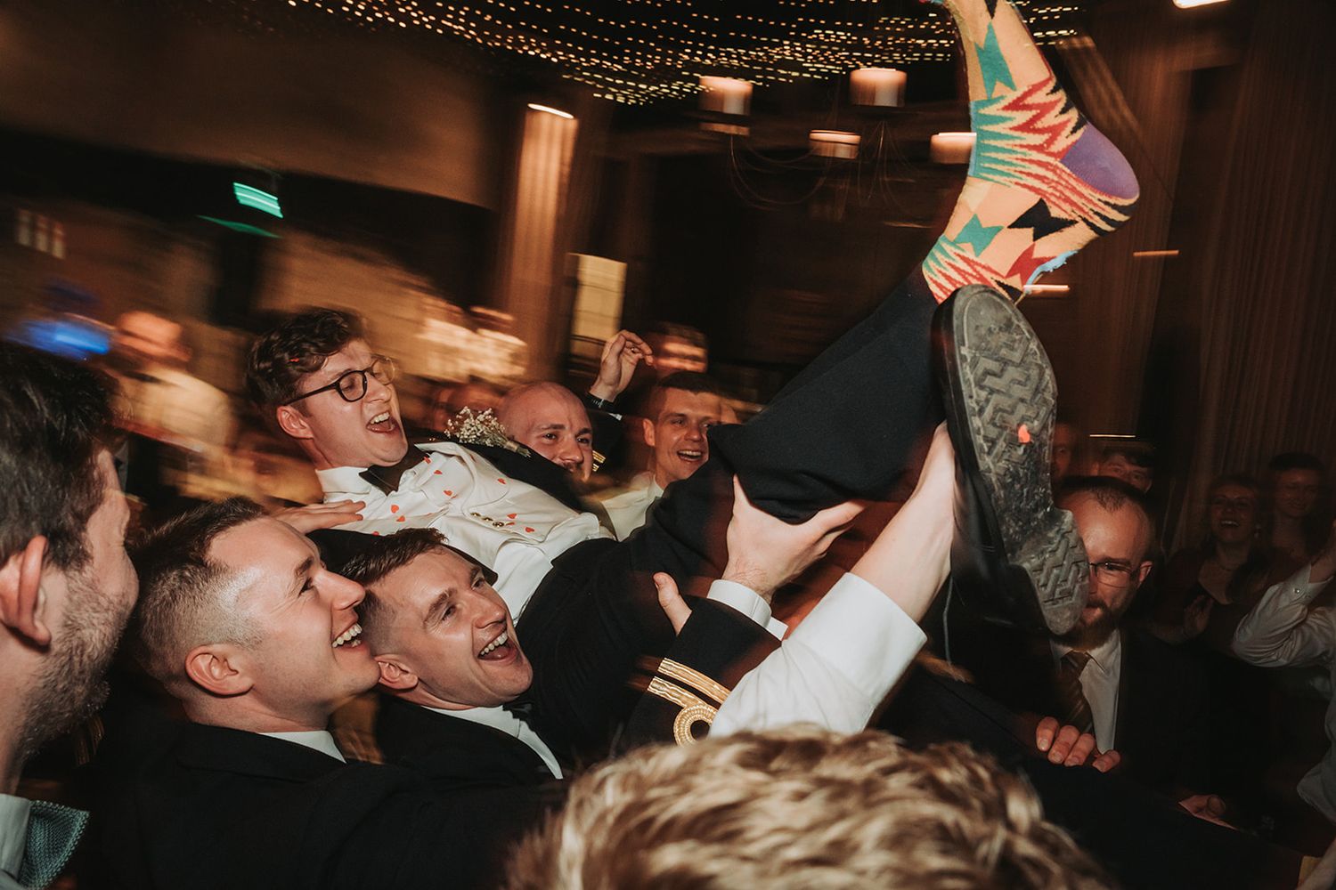Energetic crowd surfing at a concert venue with excited audience members holding up a performer in dim lighting.