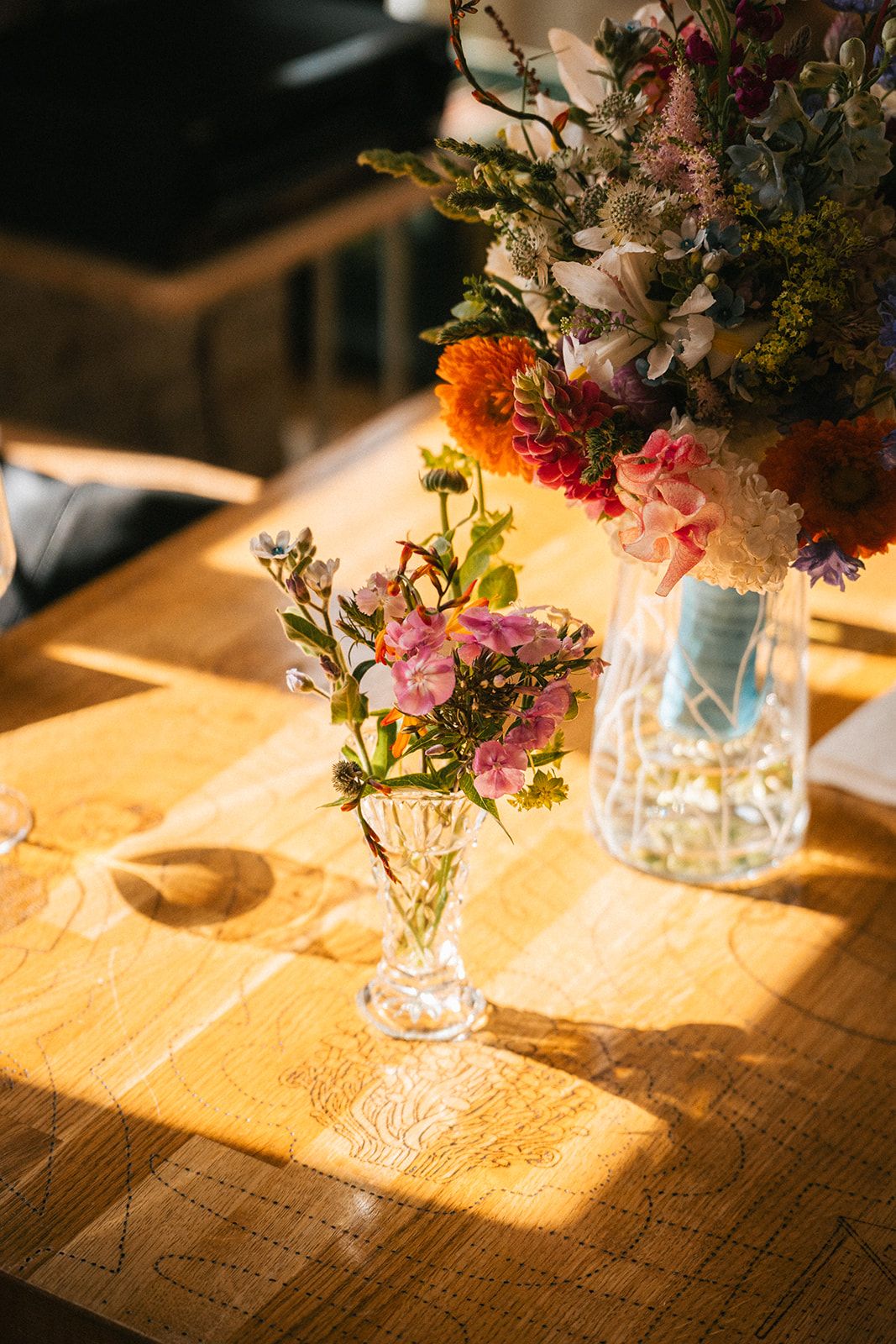 Pink floral centerpieces in glass jars cast warm shadows on a rustic wooden table in golden evening light.