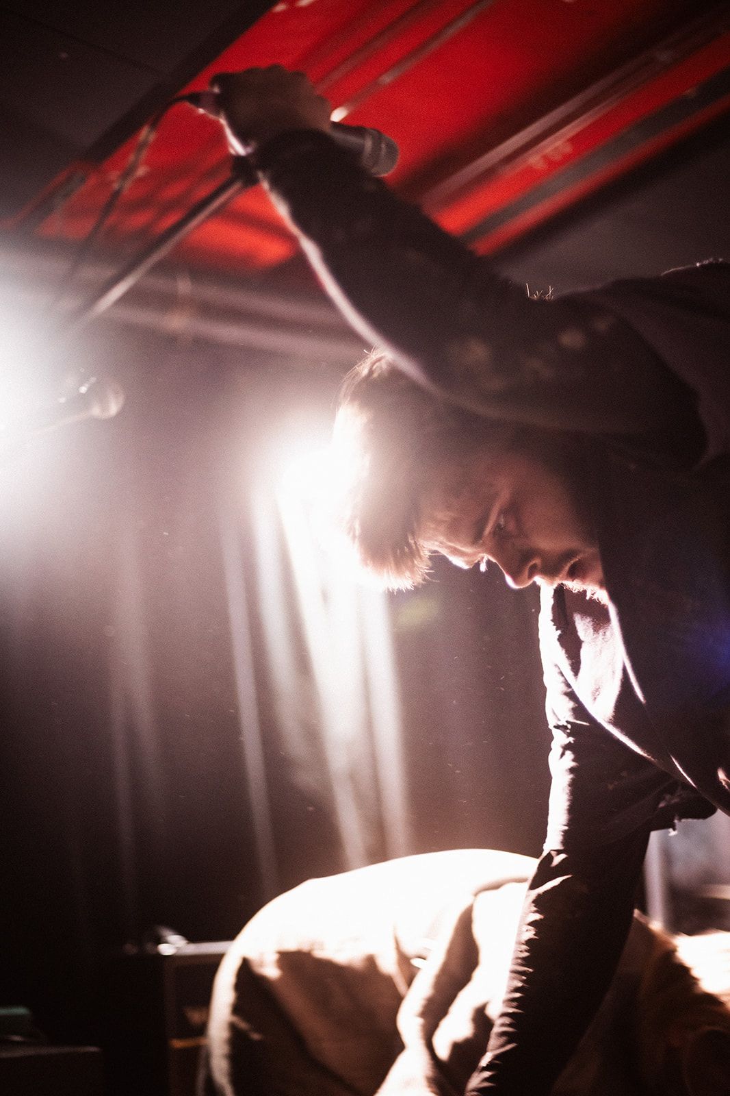 Silhouetted performer on stage dramatically backlit by bright spotlights casting dramatic shadows during concert performance.
