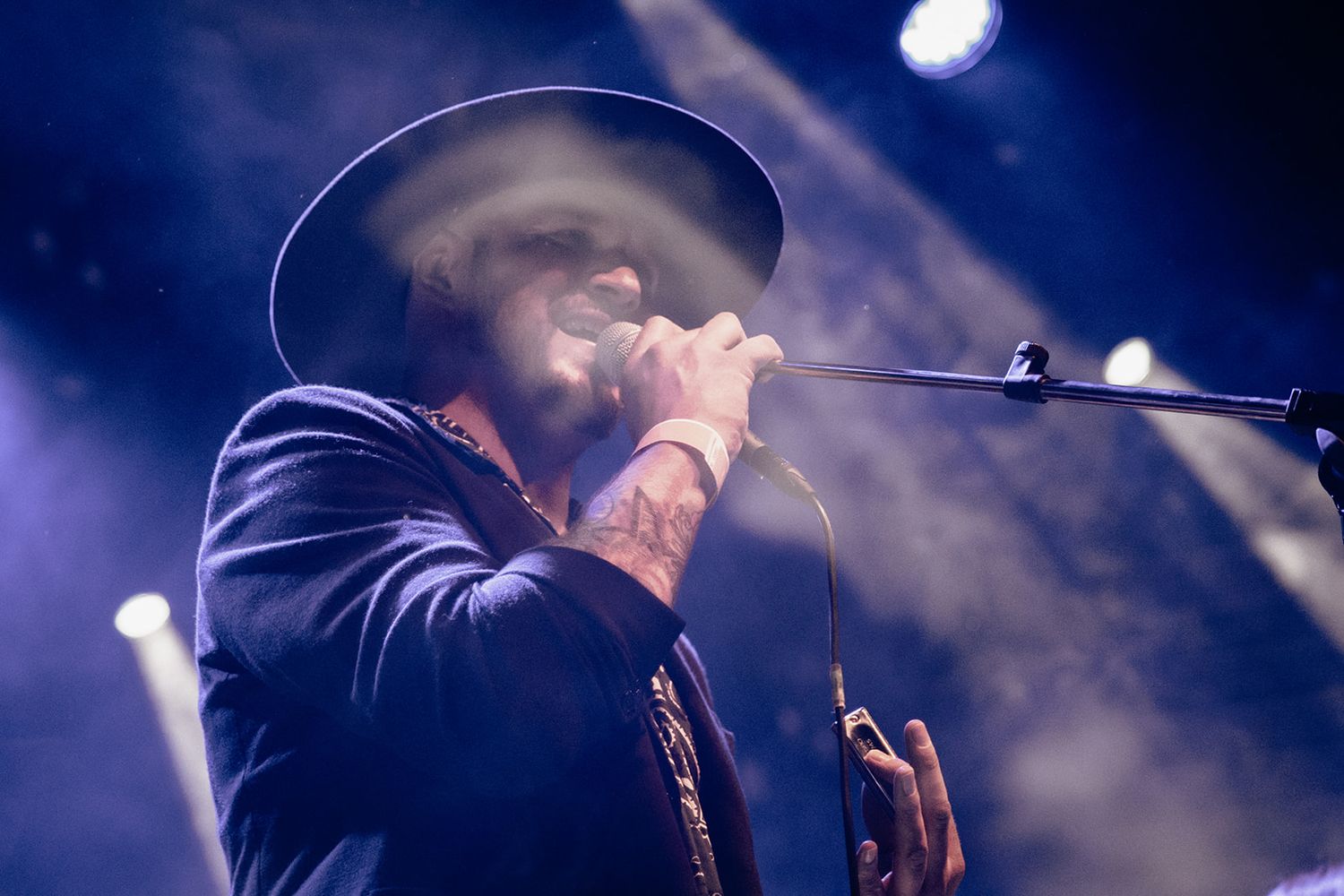 A performer in a black hat sings into a microphone on stage with dramatic backlighting and smoke effects.