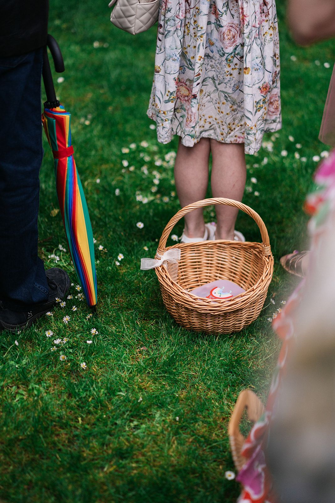 Wicker basket with a rainbow ribbon stands on green grass during an outdoor event.