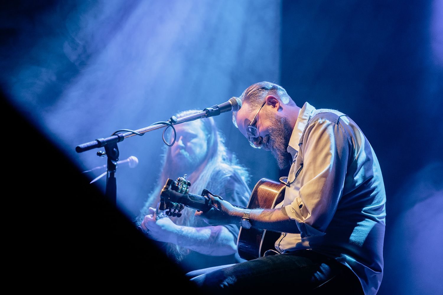 A musician performs on stage with a guitar under dramatic blue lighting during a live concert performance.