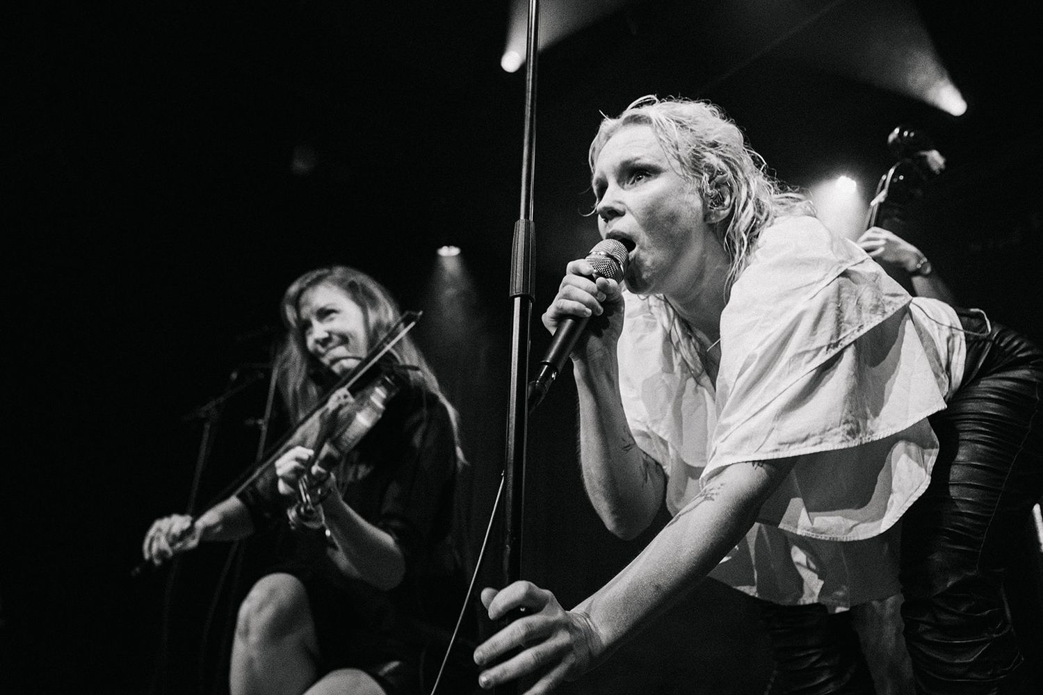 Black and white photo of two performers on stage, one playing guitar while another energetically sings into a microphone.