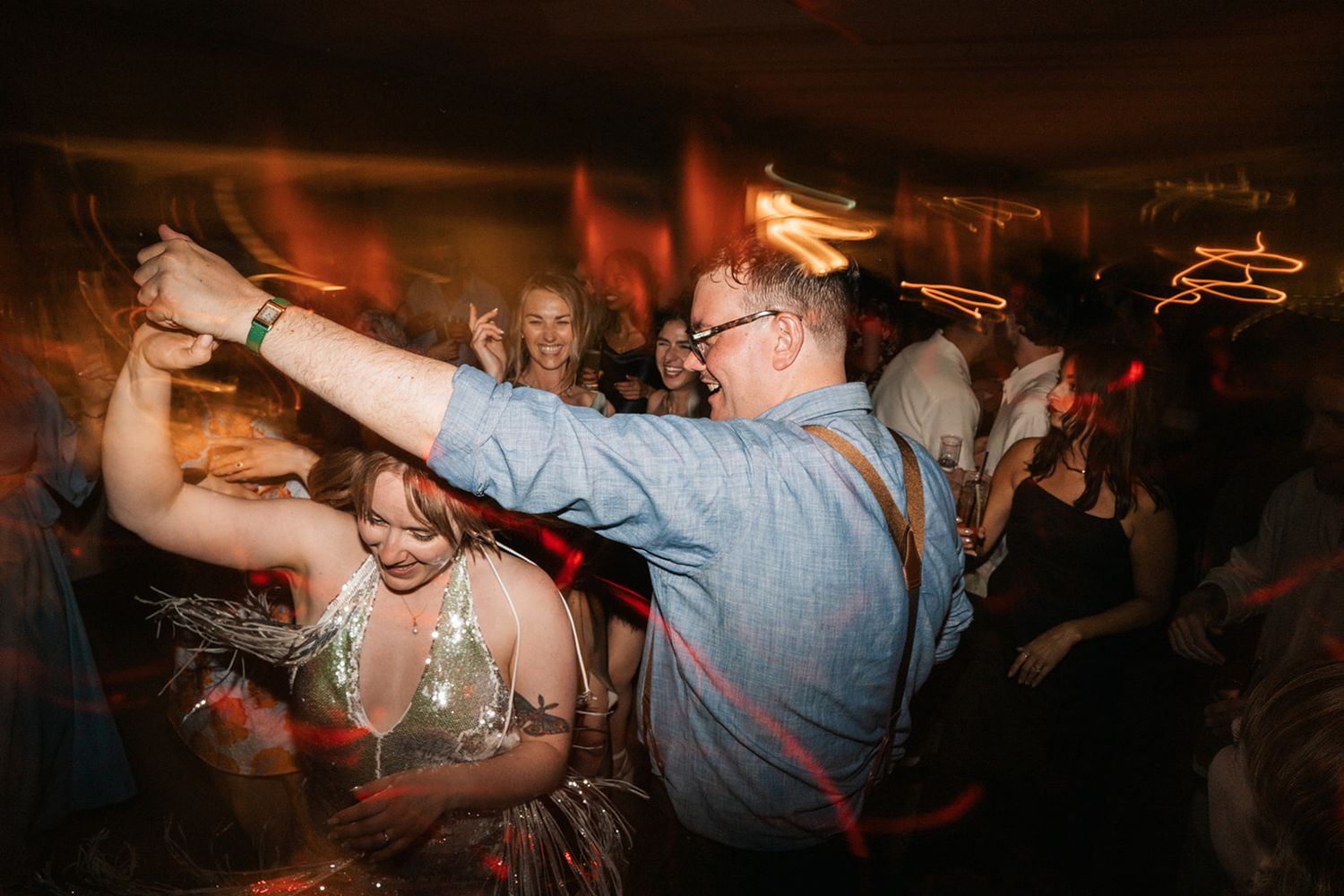 Energetic party scene on a dance floor with people dancing enthusiastically in a dimly lit venue.