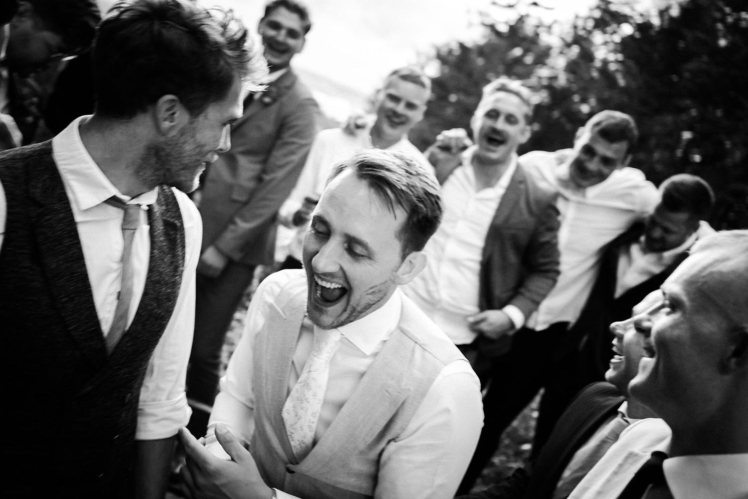 A candid black and white photo capturing laughter and joy among a group of people at a formal gathering.