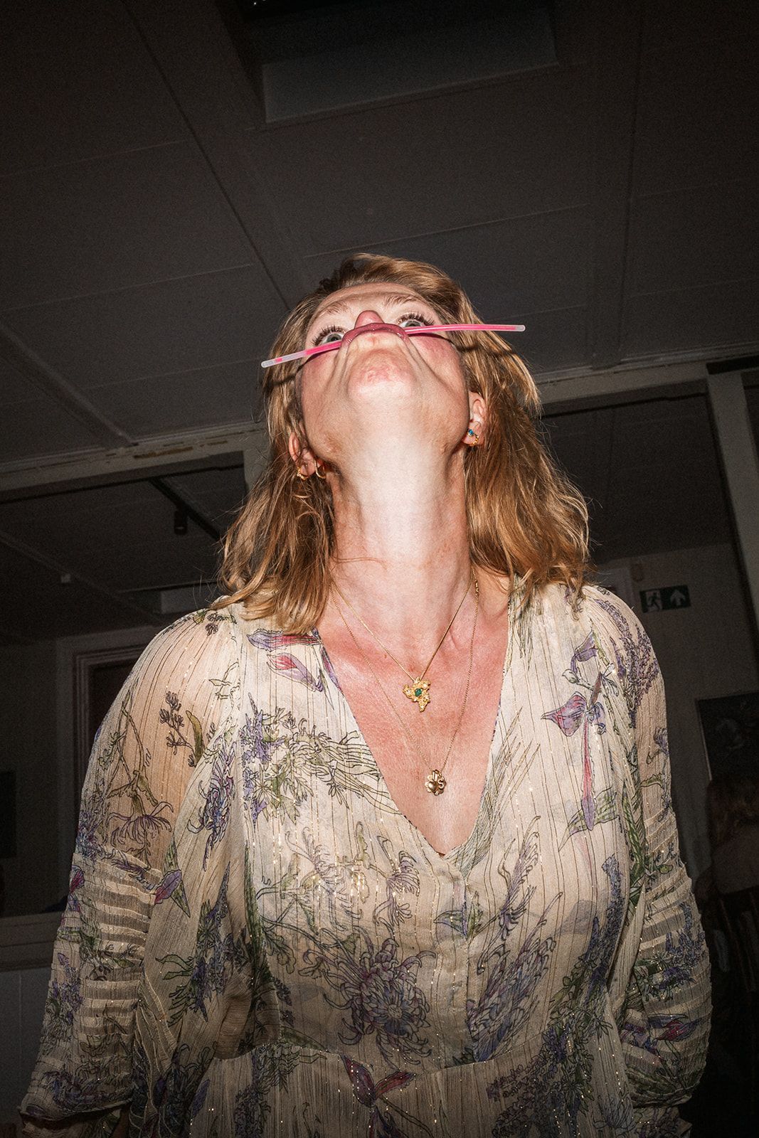 Person in patterned blouse making exaggerated expressions in dark indoor setting.