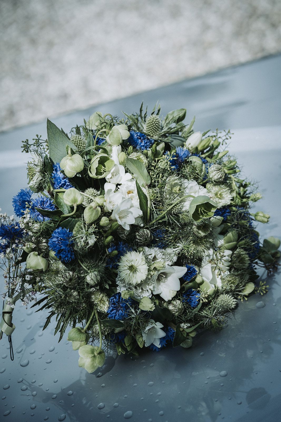 A elegant floral arrangement featuring white and deep blue flowers with greenery displayed on a reflective surface.