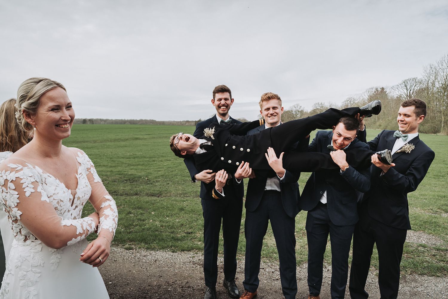 Wedding party members pose with style and humor on a grassy hillside during an outdoor celebration.