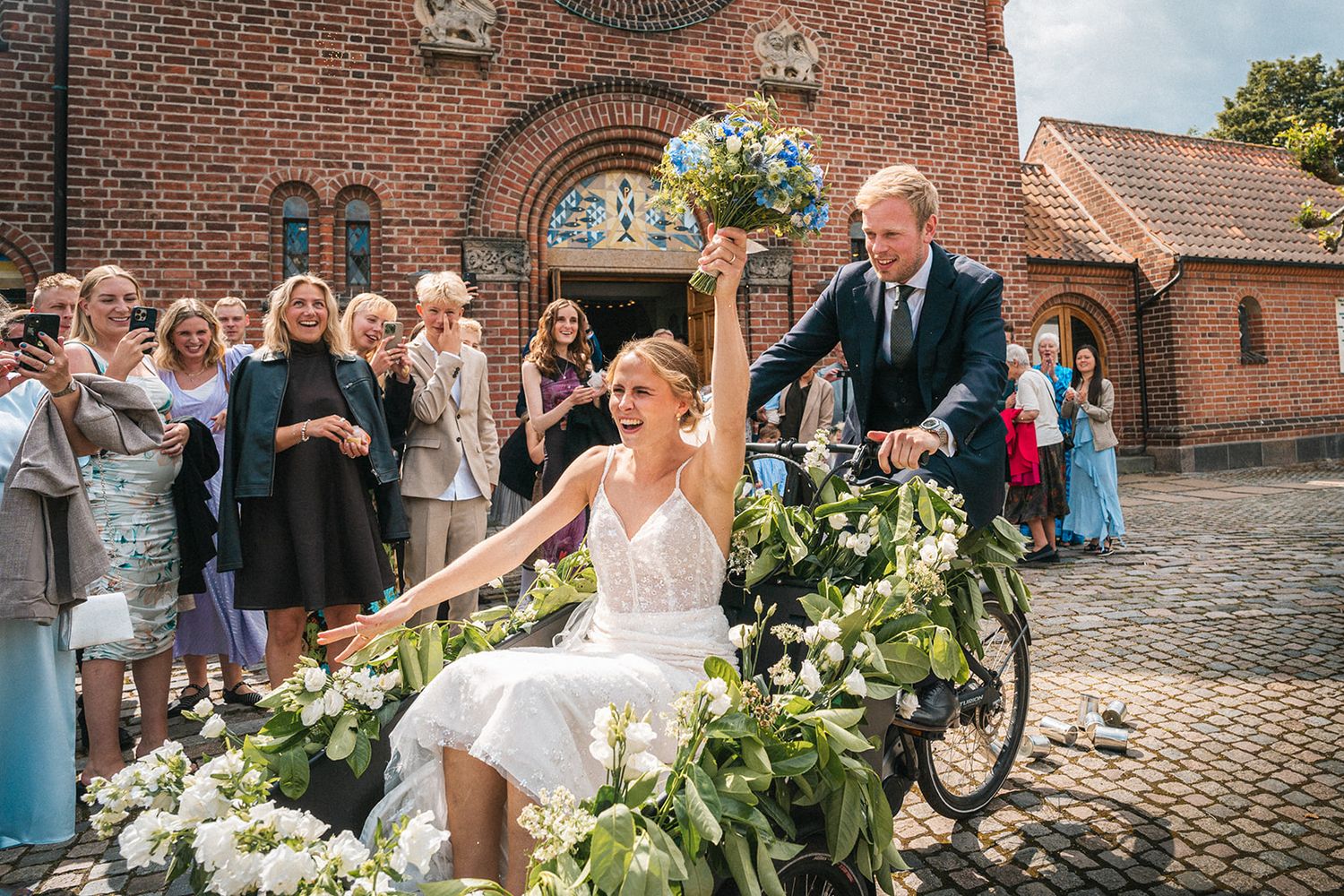 A charming wedding scene outside a brick church with a decorated bicycle as festive transportation for the newlyweds.