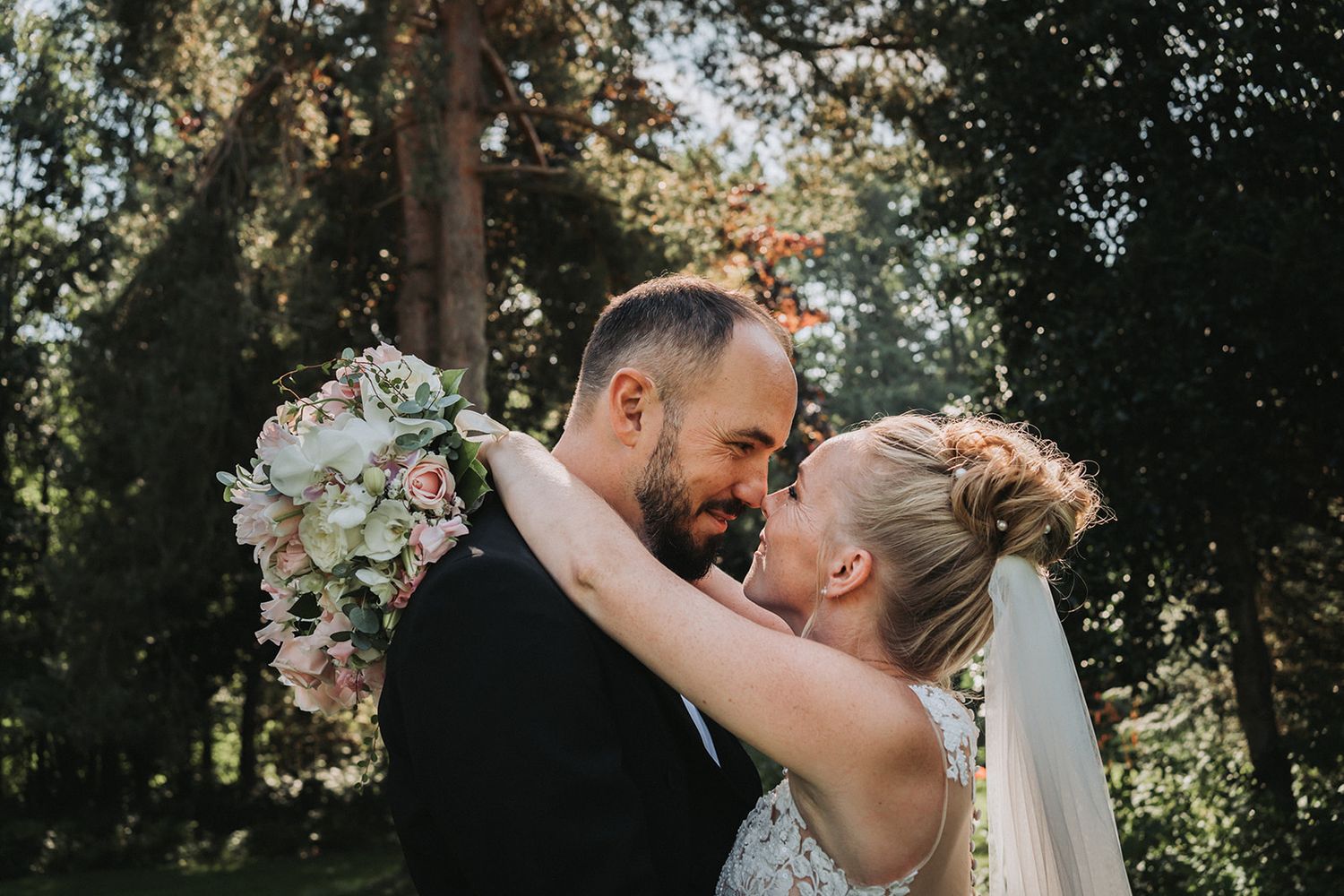 A romantic wedding couple shares intimate moments in a lush green forest setting.