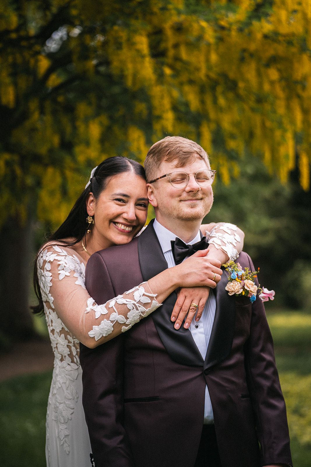 A joyful wedding couple embraces outdoors with golden autumn foliage creating a warm romantic backdrop.