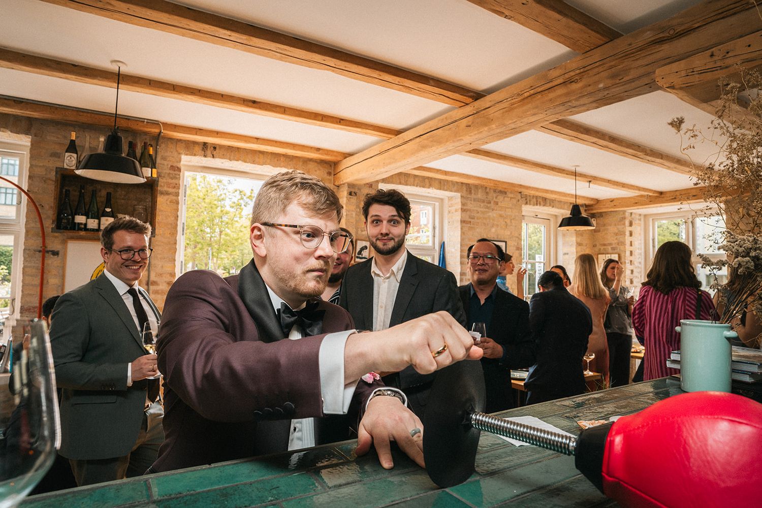 A group of people gather around a table with a red ball in a rustic room with exposed wooden beams and natural light.