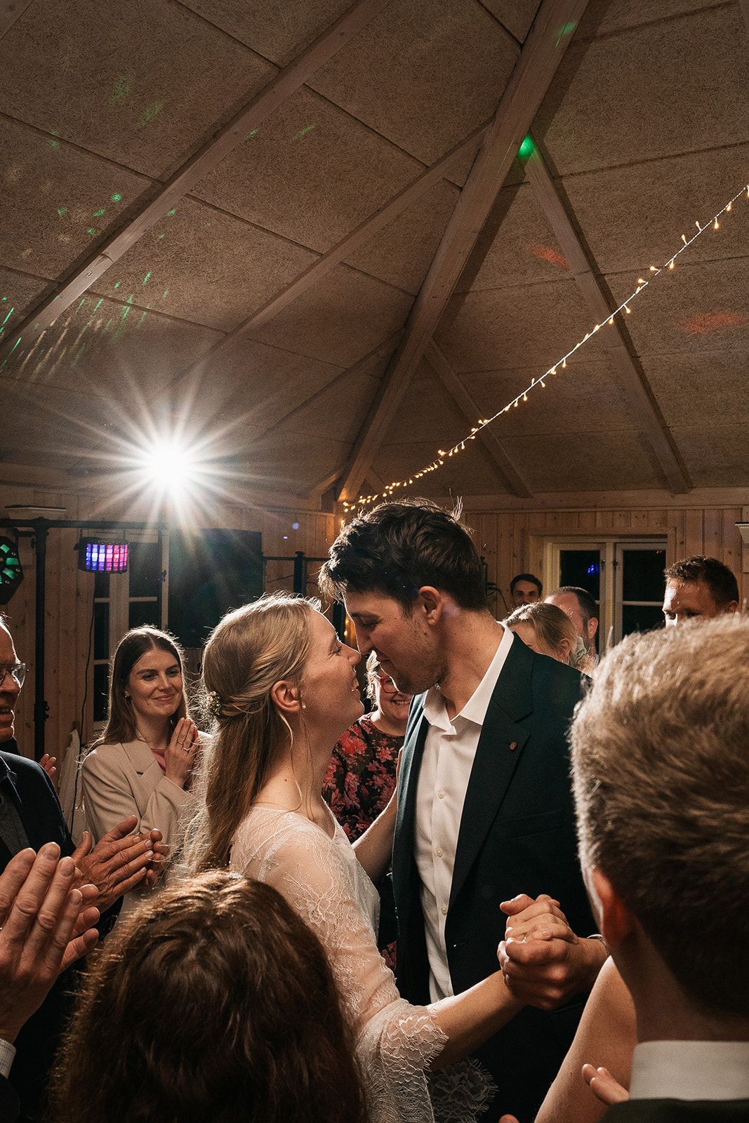 A romantic moment captured on a dance floor under twinkling lights as couples dance at an indoor reception venue.