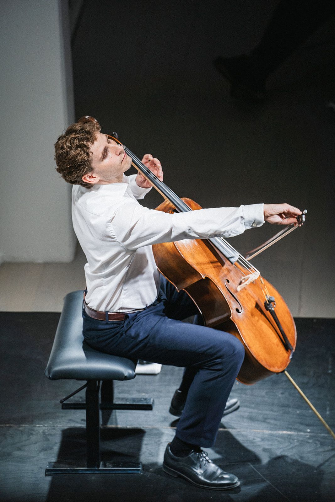 Sequential photos show a cellist performing with dramatic movement while seated on a black chair against a dark background.