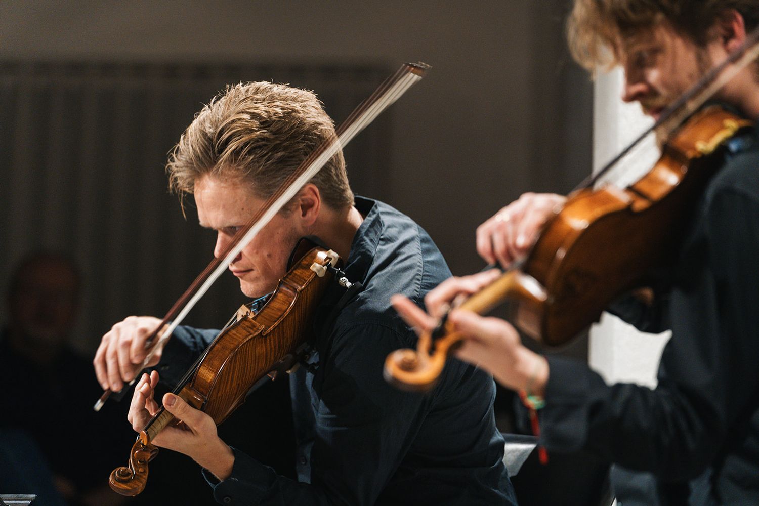 A classical orchestra performs on stage, with close-up shots of violinists playing their instruments in dramatic lighting.