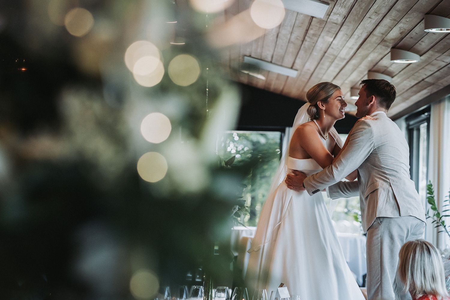 Wedding party celebrates with champagne glasses on an outdoor covered patio with bokeh lights in background.