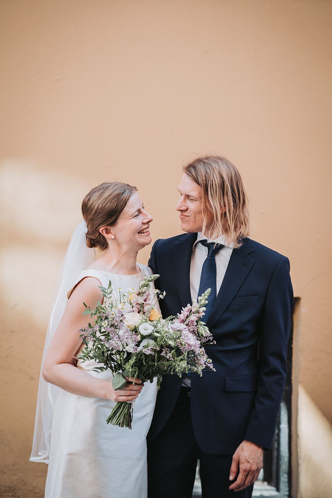 A joyful wedding couple sharing a candid moment together while the bride holds a beautiful bouquet of flowers.