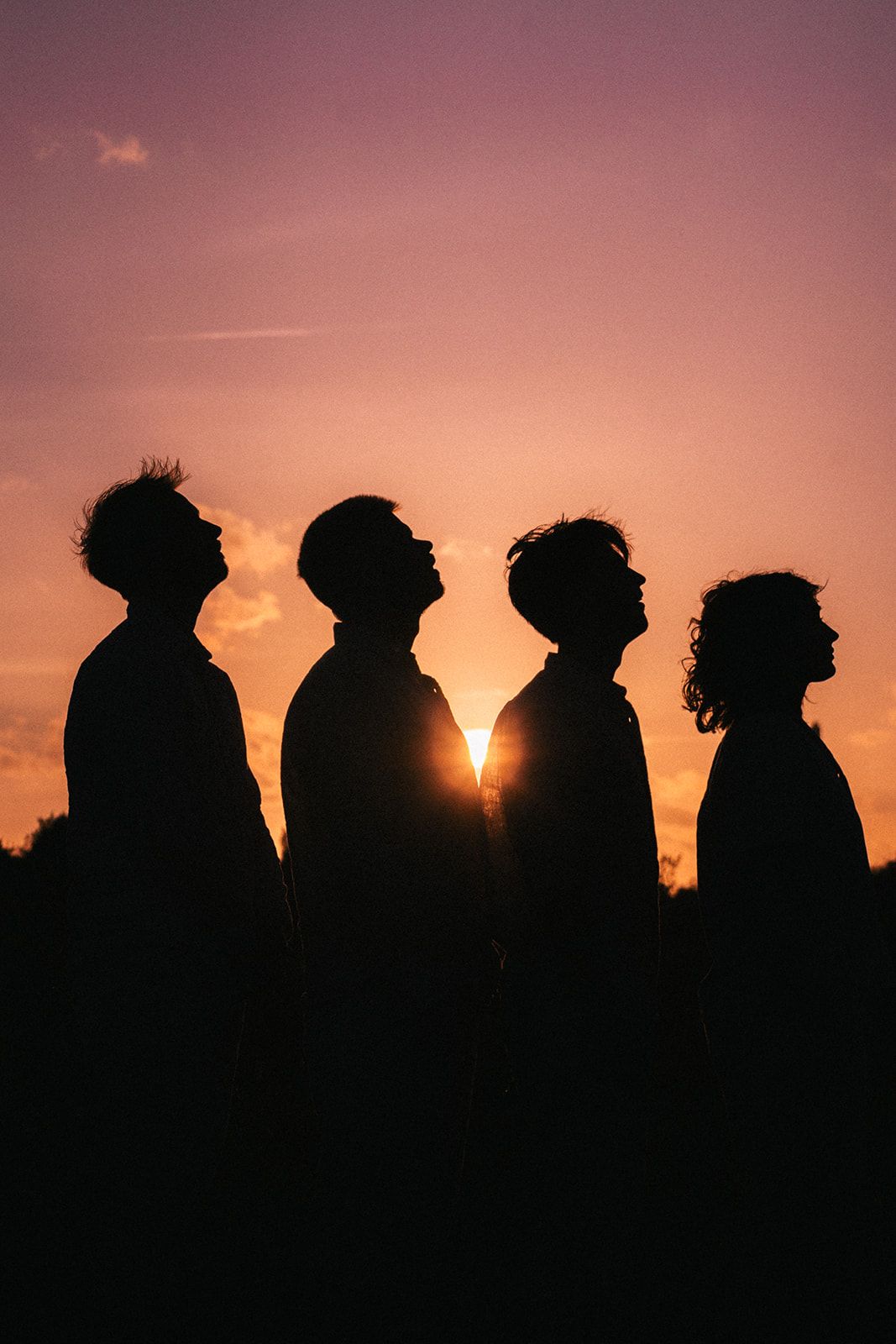 Silhouettes of four people looking up against a warm orange sunset sky with the sun peeking through their profiles.
