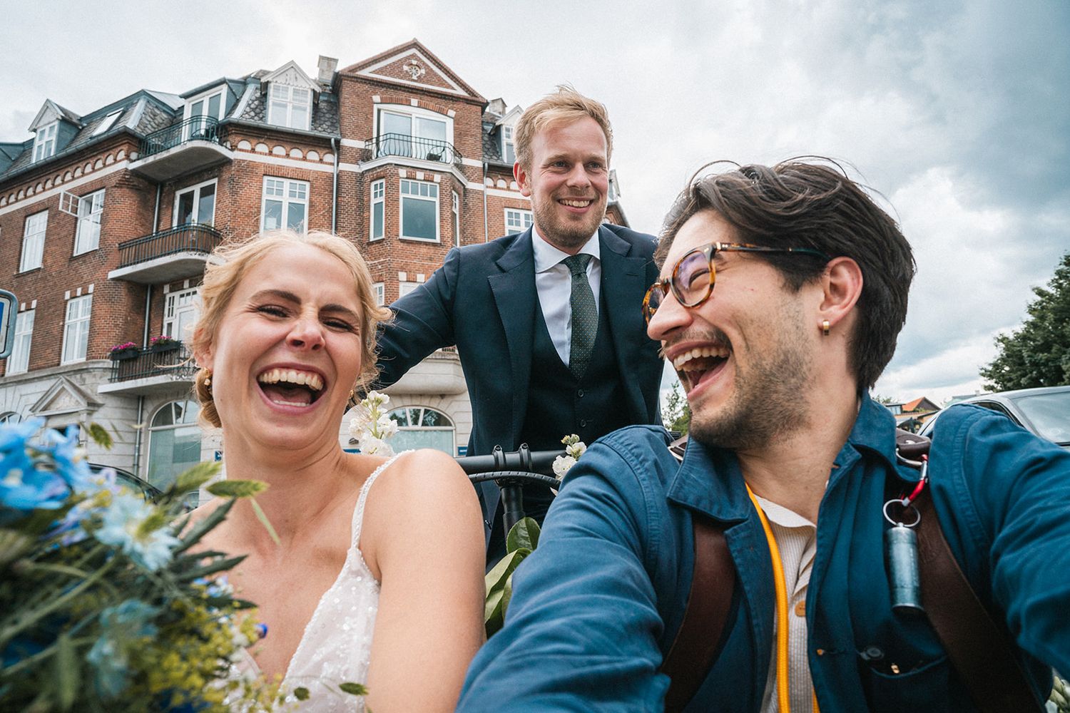Three people enjoying a candid moment outdoors with laughter and smiles in front of a brick building.