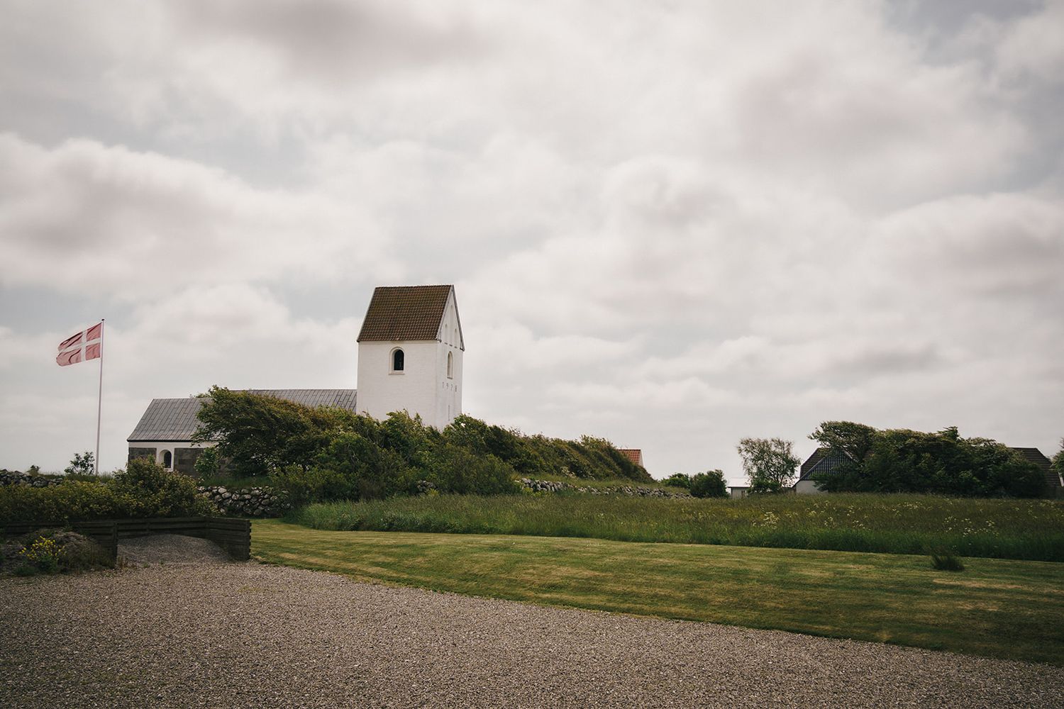 White church building with Danish flag on a hill under cloudy skies in rural Denmark.