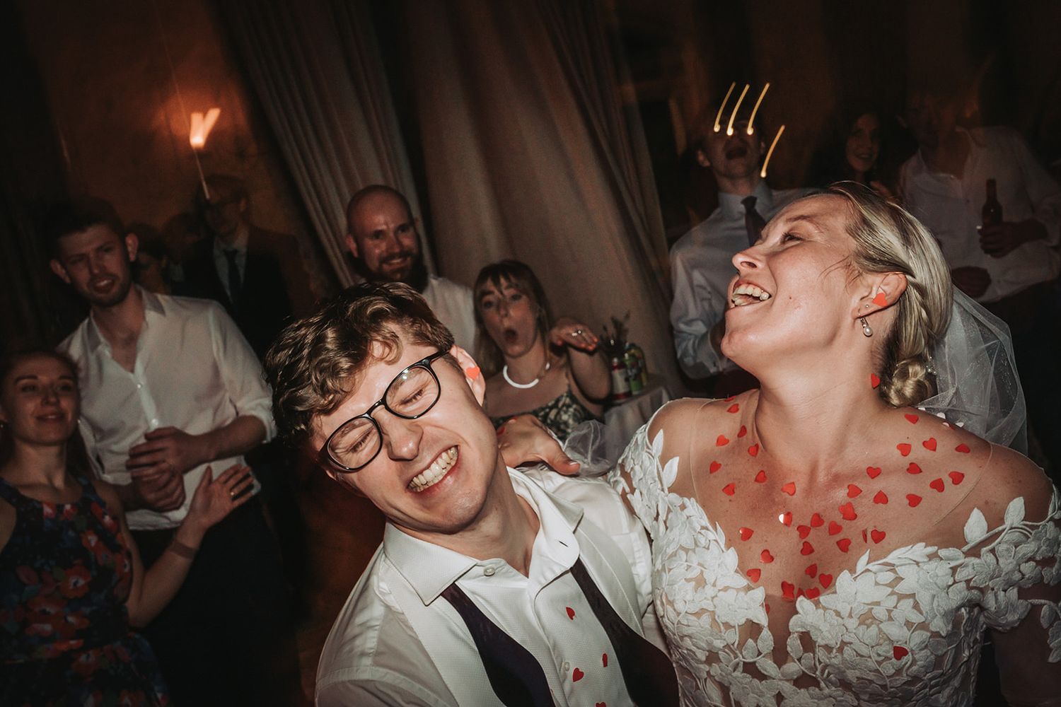 Laughing people dancing together at a wedding reception party in a dark venue with vibrant lighting.