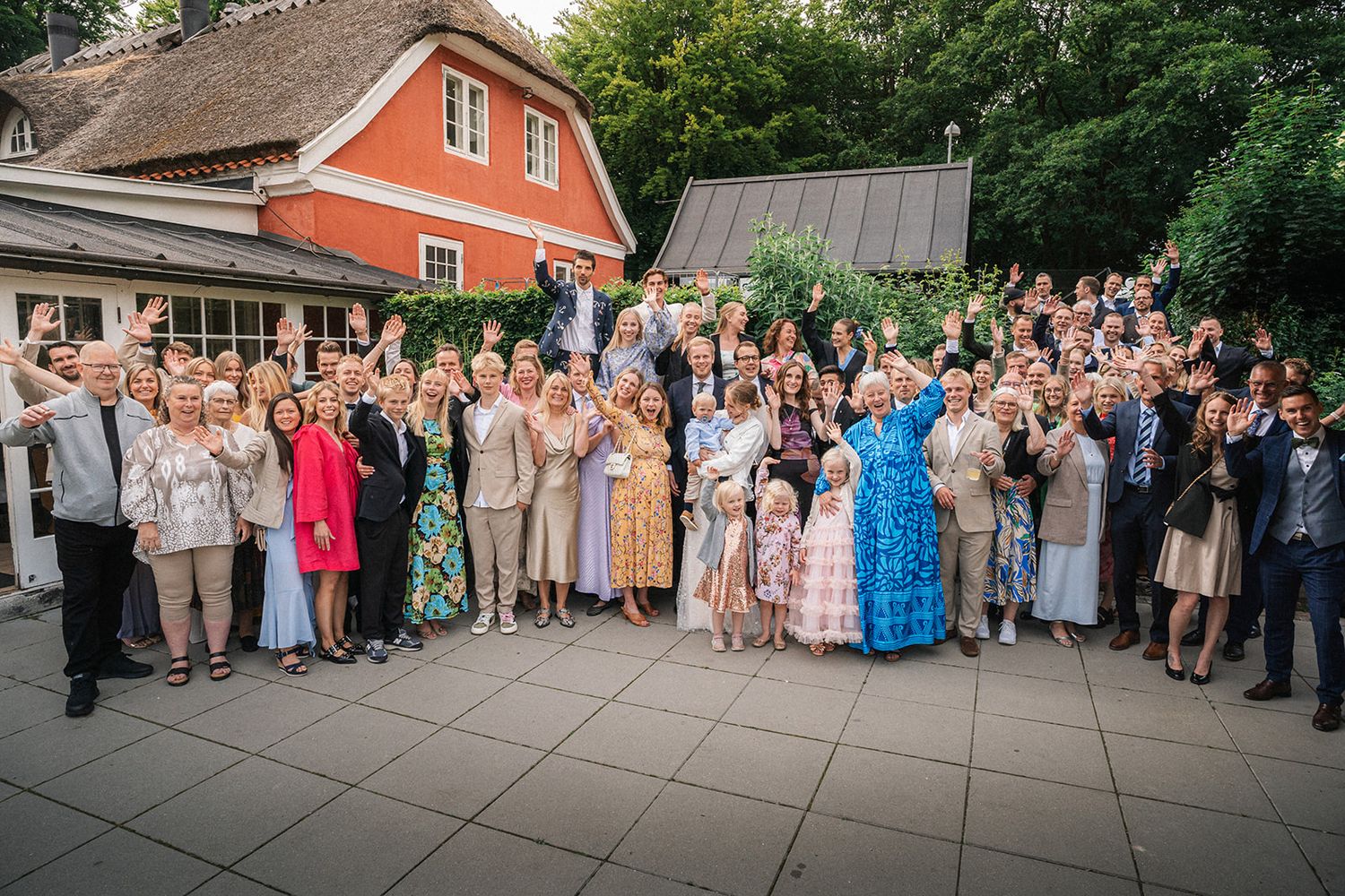 Wedding guests lined up outdoors in front of red barn for group photo during summer celebration.