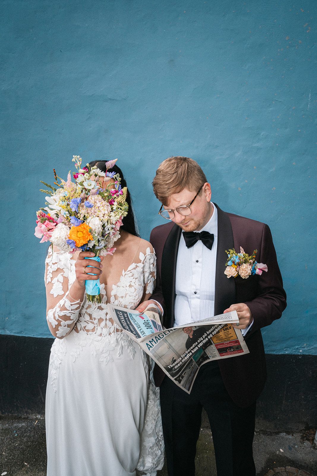 Wedding couple holding comic books while posing against a teal colored wall for a creative photo series.