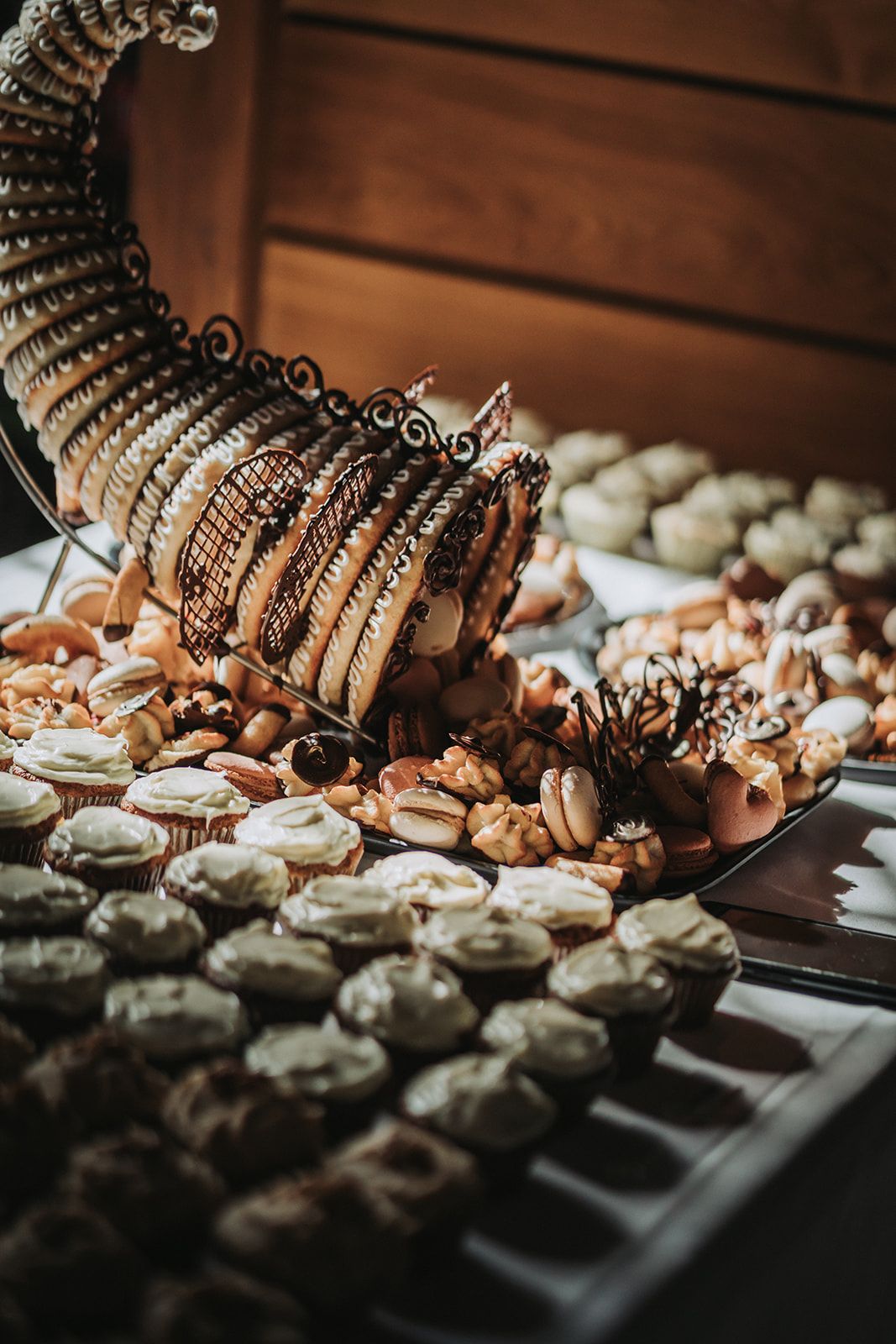 A selection of elegant wedding desserts and treats arranged on a dark wooden table with dramatic lighting.