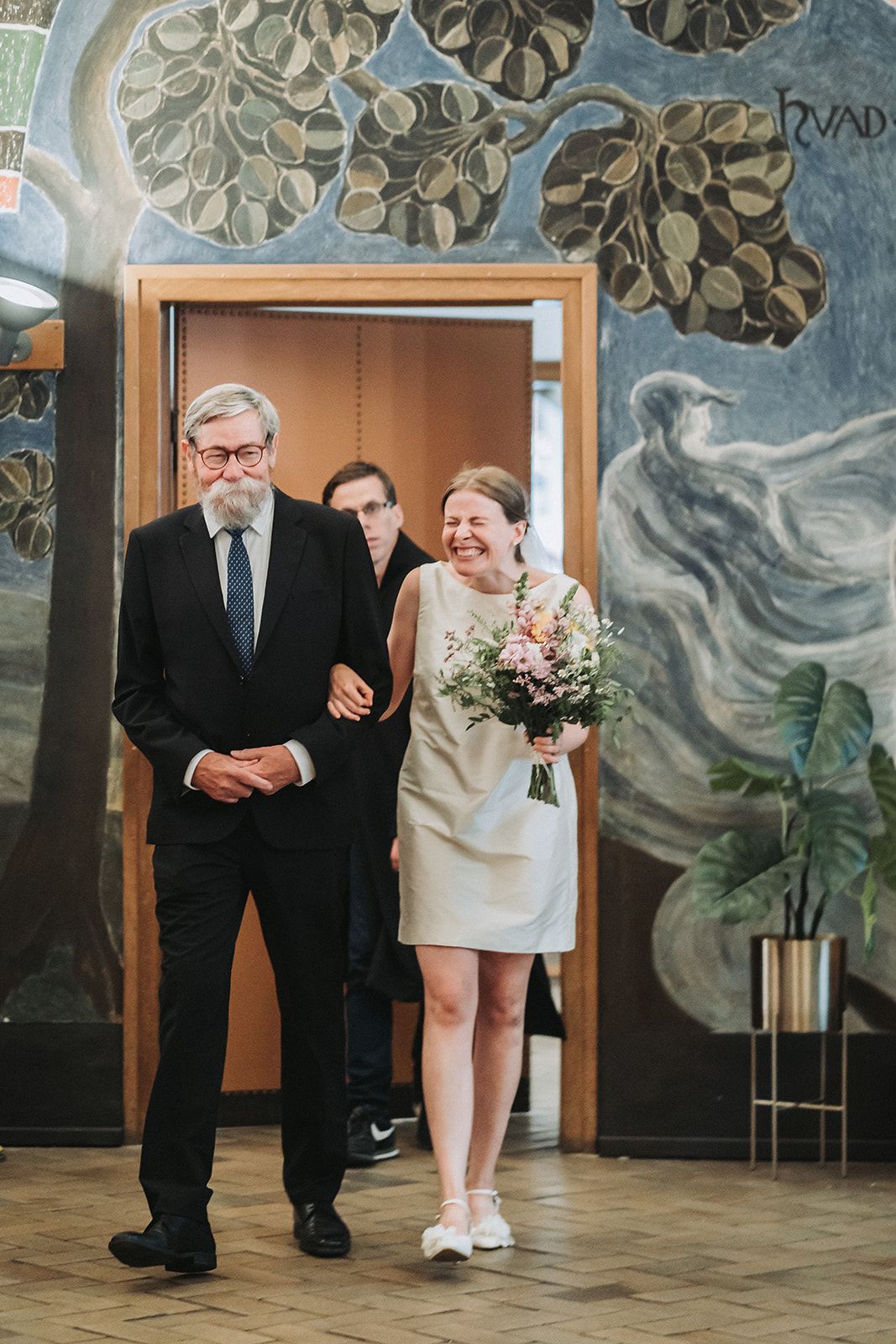 Couple walks together in an elegant room with decorative monstera leaf wall murals.