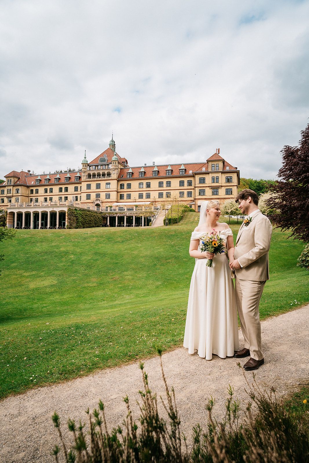 Wedding couple poses on path with grand historic building in background.
