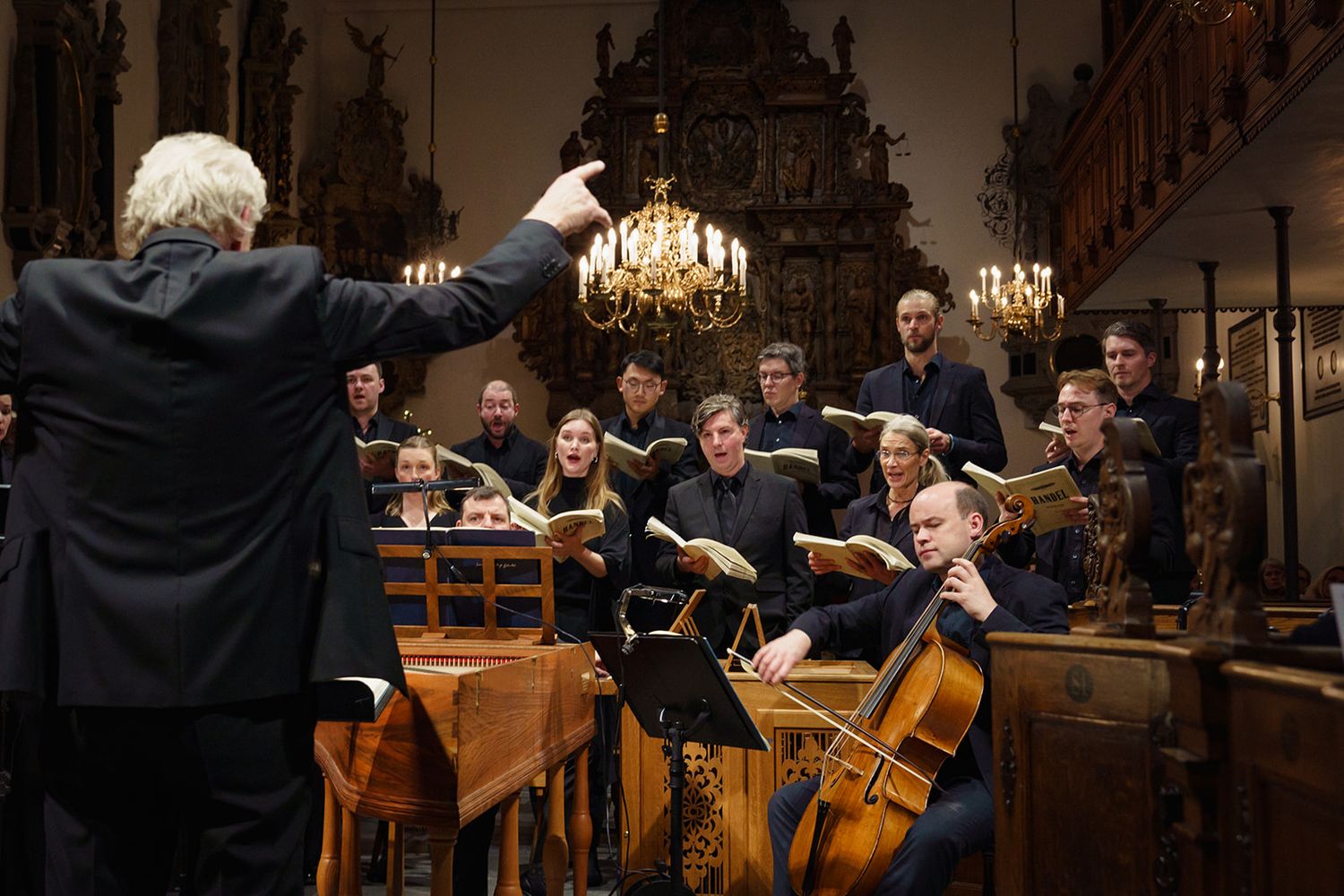 Orchestra musicians with instruments follow a conductor during a classical performance in an ornate concert hall.