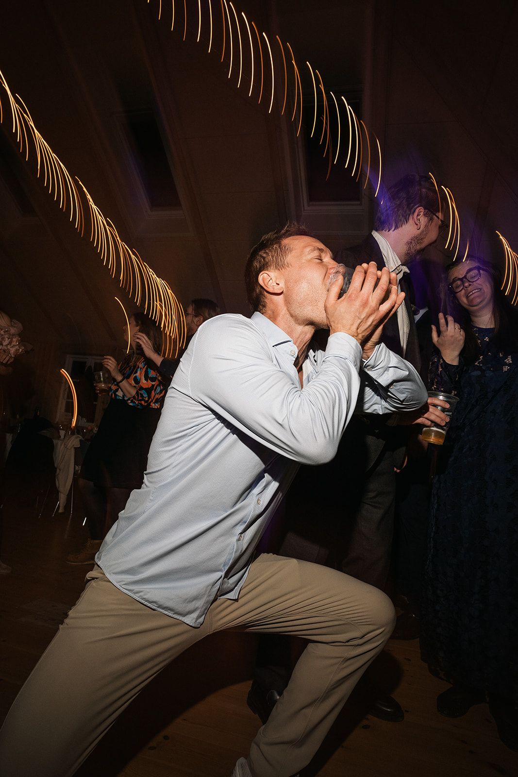 Someone in a light colored sweater dances expressively at an indoor party with palm fronds visible in background.
