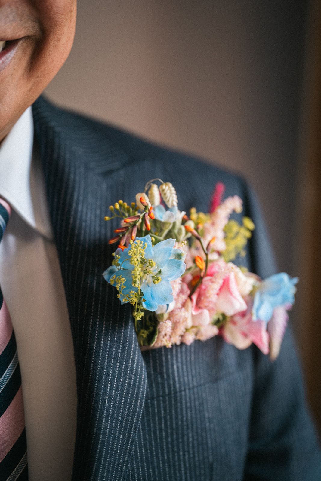 A delicate floral boutonniere with pink and blue blooms adorns a pinstriped suit jacket lapel.