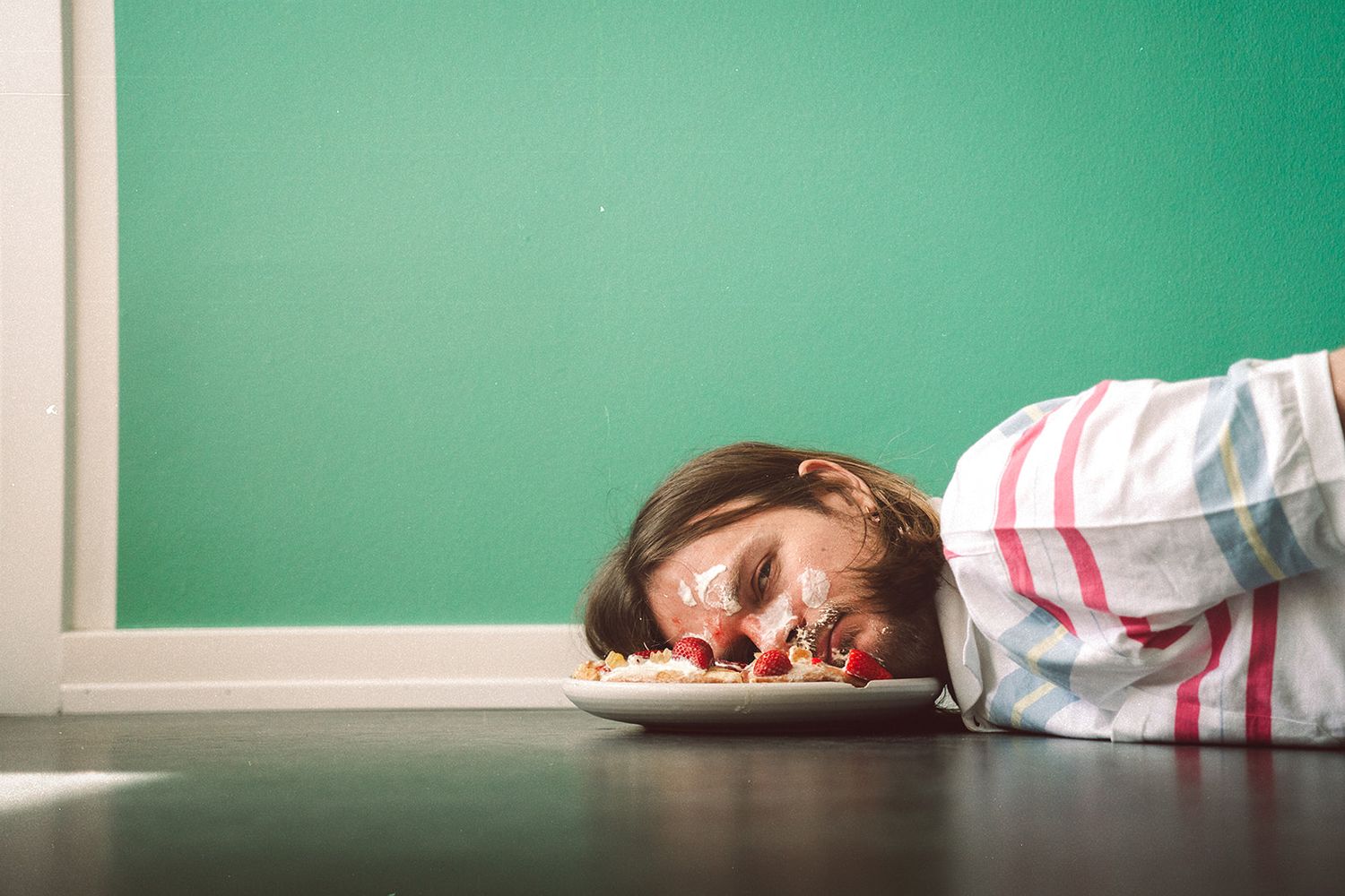 A person in a striped shirt lying asleep on a desk with a green chalkboard in the background.
