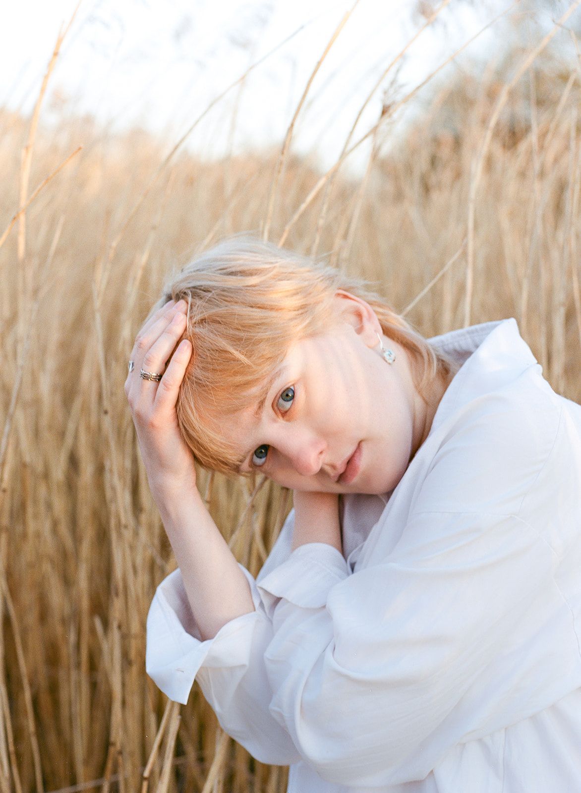 A dreamy ethereal portrait in tall wheat fields at golden hour features gentle lighting and a white flowing shirt.