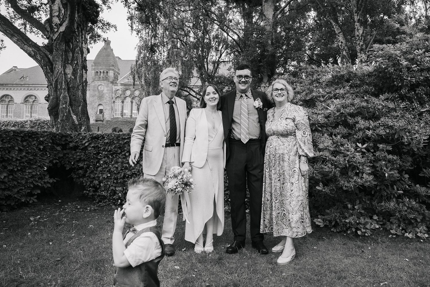 Black and white vintage photograph showing a group of people posing outdoors in formal attire with a garden setting.
