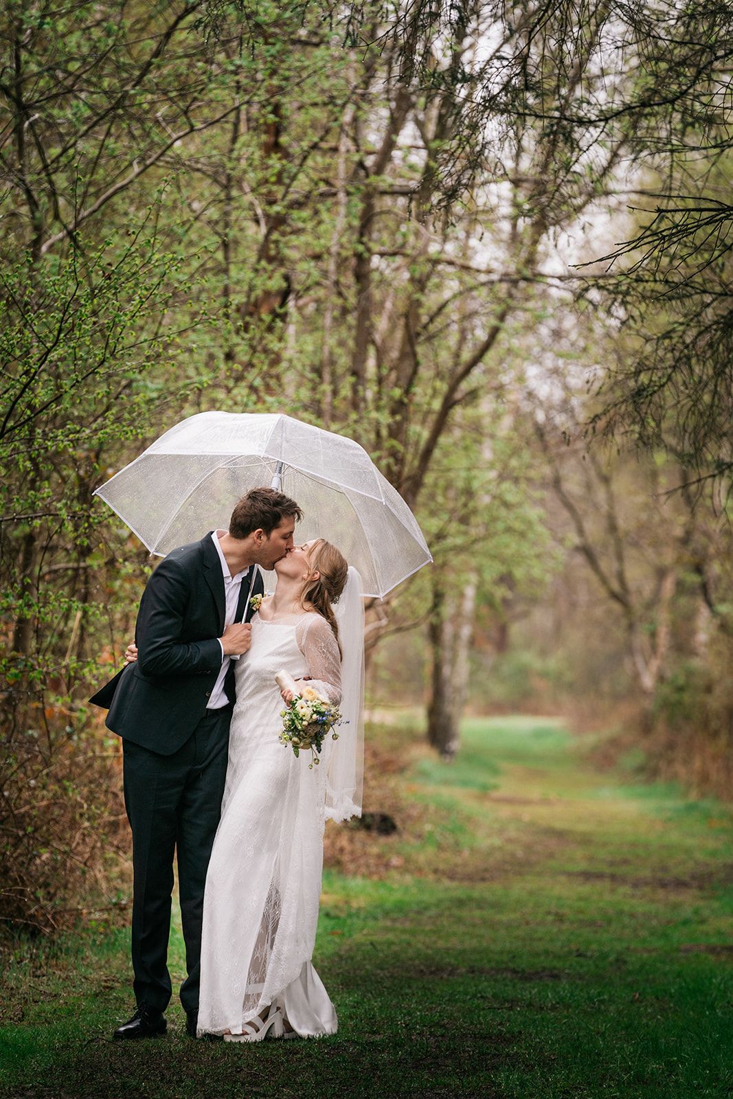 Romantic moment under white umbrella on woodland path during wedding.