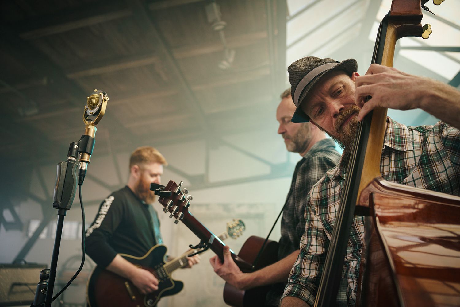 Musicians play instruments together during a recording session in a studio with natural lighting.