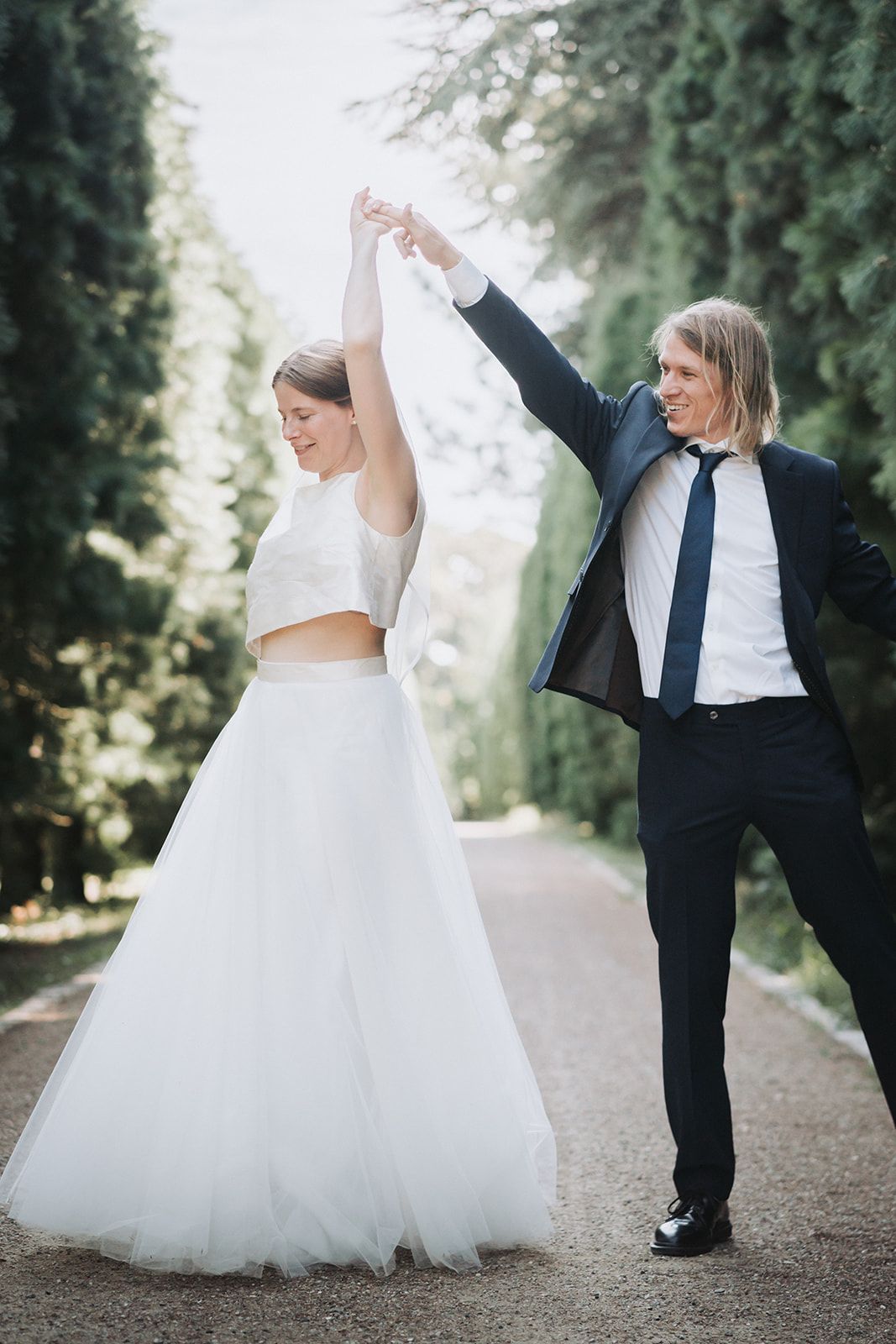 Wedding couple dances joyfully on a tree-lined path in romantic outdoor photo shoot series.