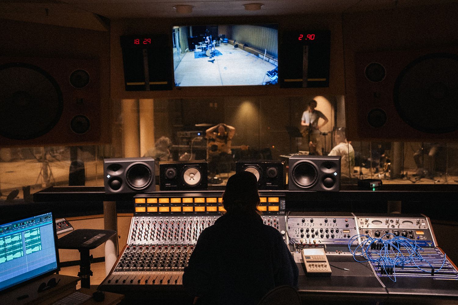 Sound engineer working at mixing console in professional recording studio with monitors and screens displaying audio tracks.