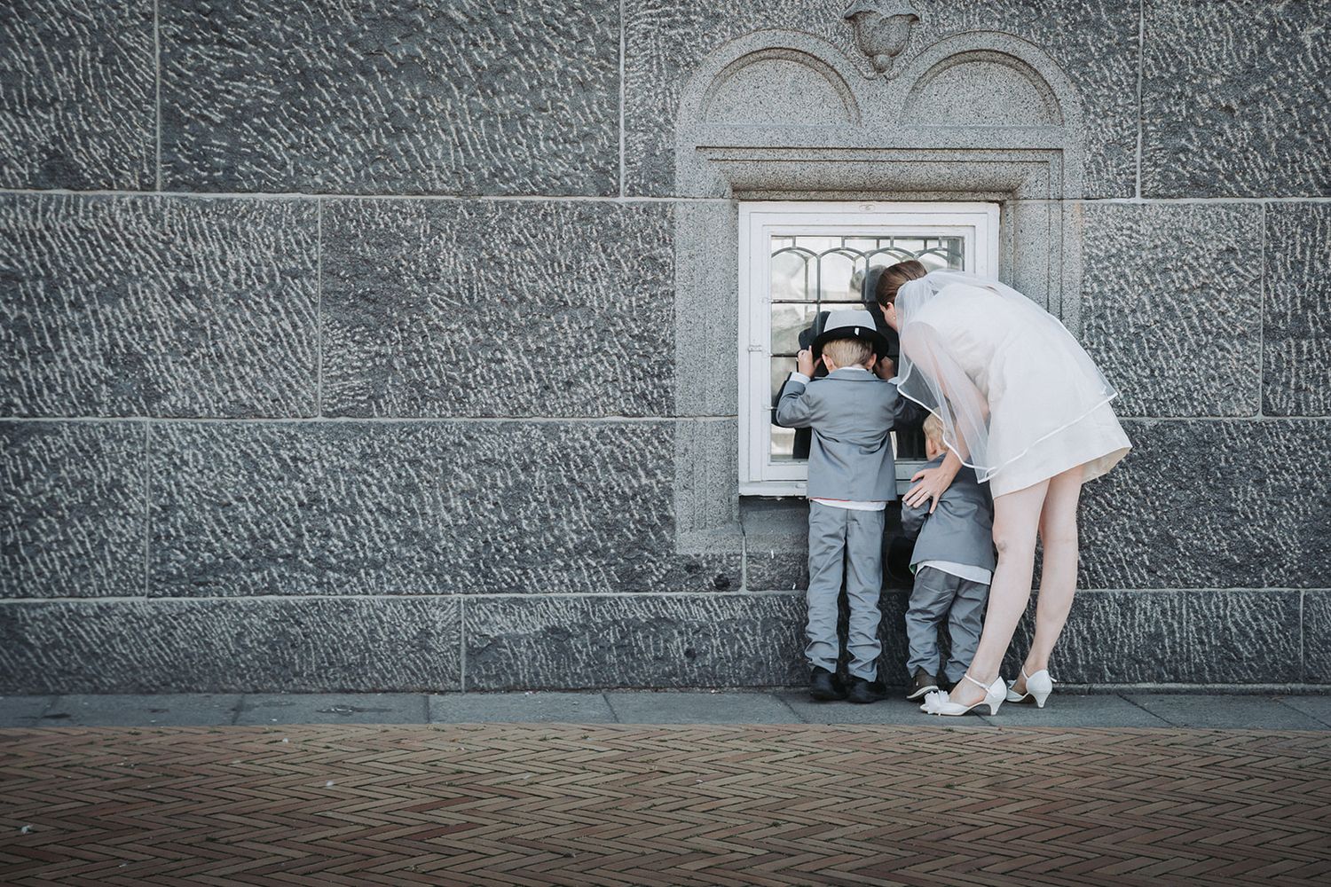 Child and adult peering through a small window in a grey stone wall together during a playful moment.