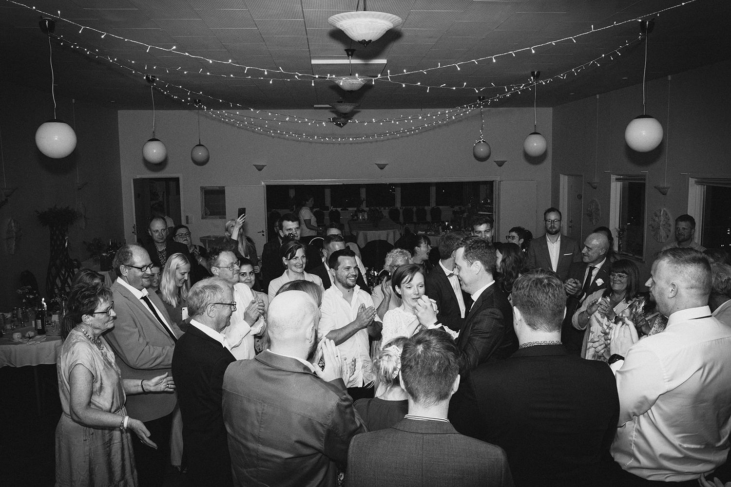 Vintage black and white photograph of people gathered at an indoor social event with string lights and round paper lanterns.