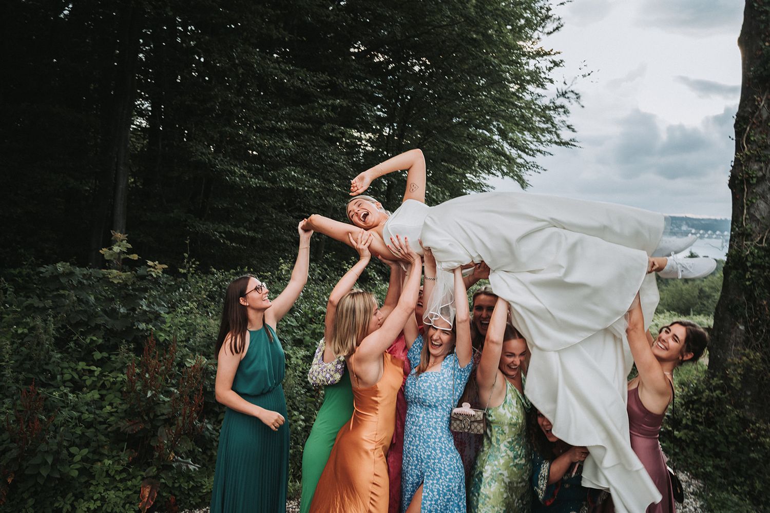 Group of bridesmaids in colorful dresses dancing together at outdoor wedding celebration.