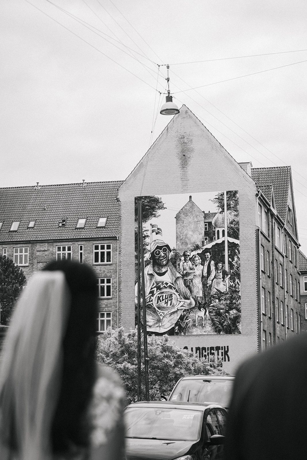 Black and white urban street scene showing apartment buildings with graffiti art murals on their facades.