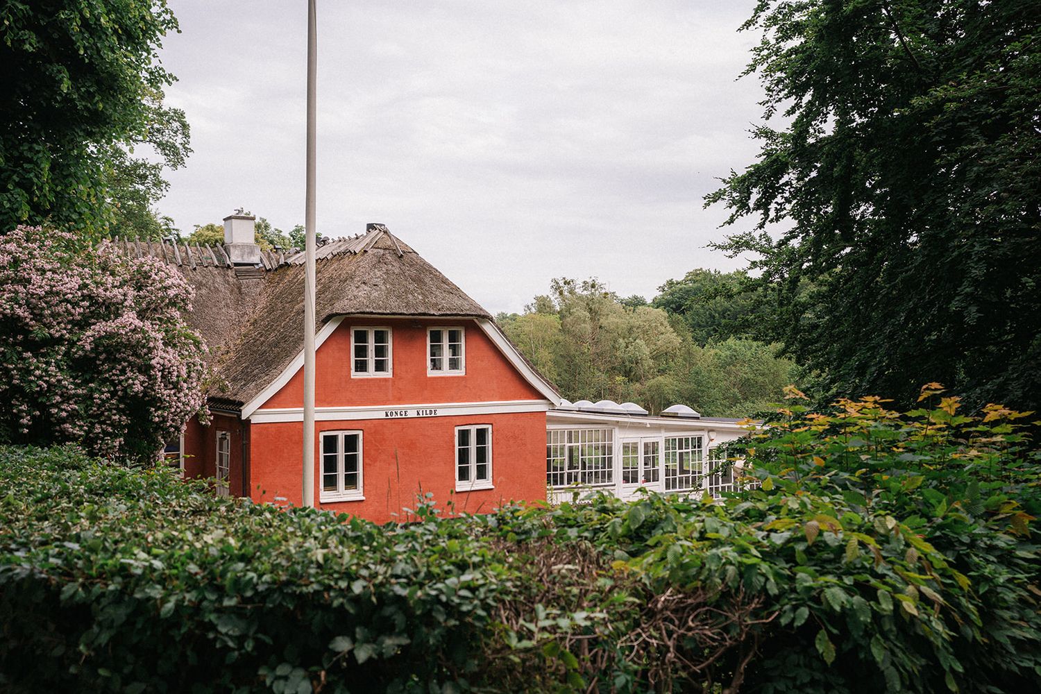 A series of red Swedish-style cottages with white trim nestled among lush green gardens and trees.