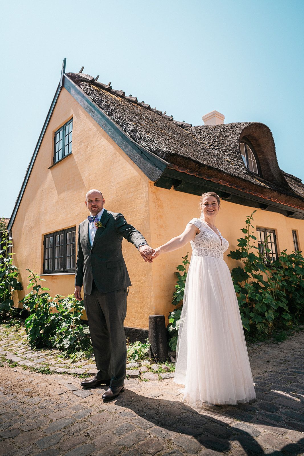 A playful wedding photoshoot outside a peach-colored building with cobblestone ground.